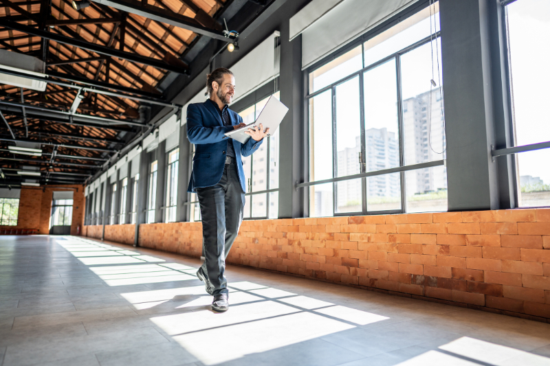 Mature businessman walking and using laptop at empty office for sell at real estate